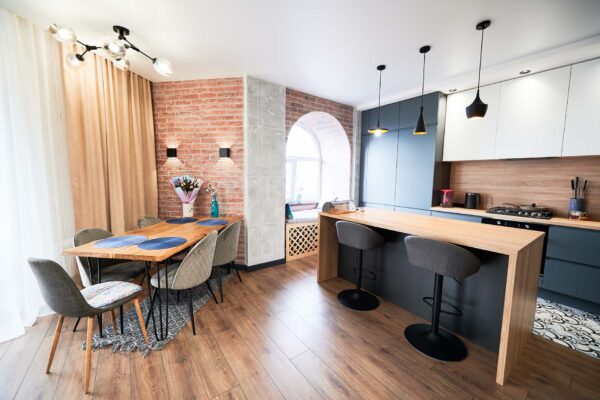 Living room and kitchen studio in dark blue color with modern furniture table, chair and stylish lamps. Concept of stylish modern interior kitchen with bar table.